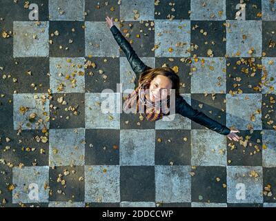Smiling woman with arms outstretched spinning on asphalt painted with checked pattern