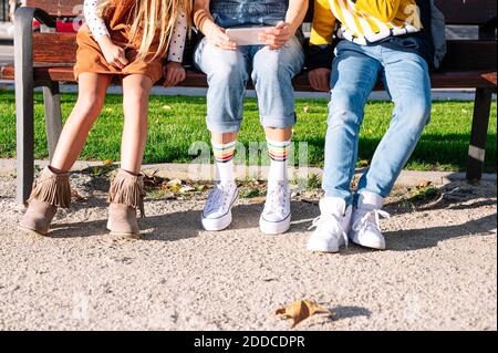 Low section of mother with kids using smart phone sitting on bench in public park during sunny day Stock Photo