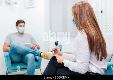 Doctor writing in notepad while listening to patient problem at office Stock Photo