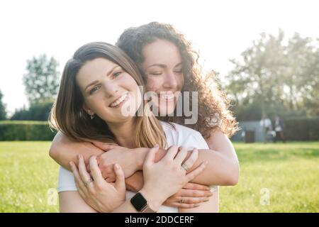 Beautiful woman being hugged from smiling young female friend at park Stock Photo