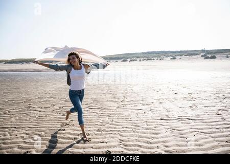 Carefree woman running while holding blanket at beach on sunny day Stock Photo