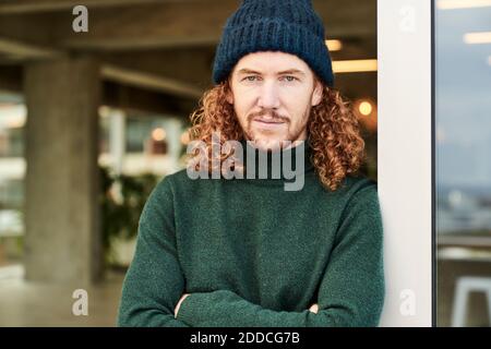 Handsome male hipster wearing knit hat while leaning on window at studio apartment Stock Photo