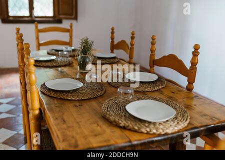 Place setting on wooden dining table with empty chairs in room Stock Photo