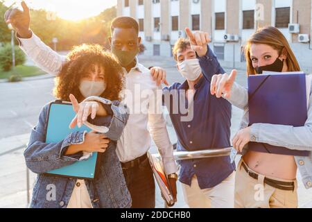 University students wearing protective face mask while pointing against education building Stock Photo