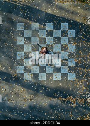Mid adult woman with arms outstretched spinning on asphalt painted with chessboard pattern