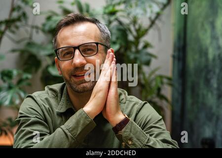 Smiling wearing eyeglasses businessman sitting with hands clasped at cafe