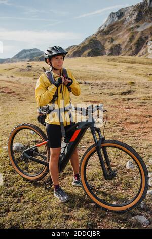 Woman in warm clothing standing on mountain bike at Somiedo Natural Park, Spain Stock Photo