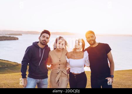 Smiling young male and female friends standing on hill against bright sky at Mirador de La Providencia, Gijon, Spain Stock Photo