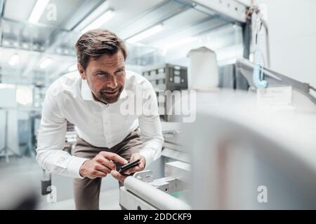 Male engineer using smart phone while examining manufacturing equipment in industry Stock Photo
