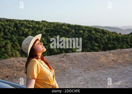 Relaxed young redhead woman leaning on car during road trip Stock Photo