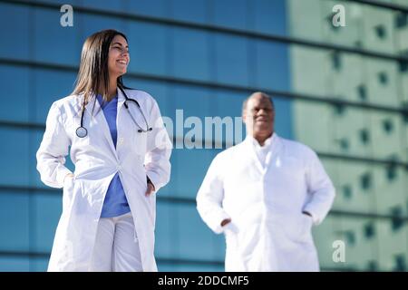 Confident doctors standing with hands in pockets against hospital Stock Photo
