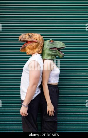 Male and female friends in dinosaur mask standing against green shutter Stock Photo