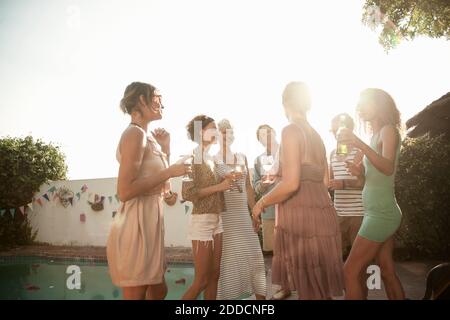 Happy friends enjoying summer while drinking alcohol at poolside against sky Stock Photo