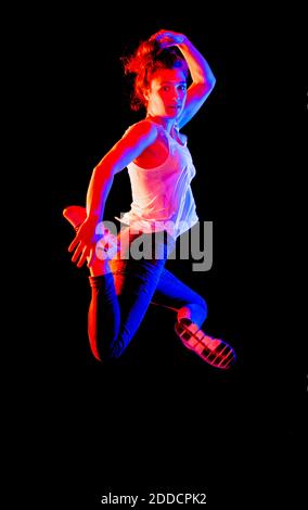 Young woman jumping in mid-air against black background Stock Photo