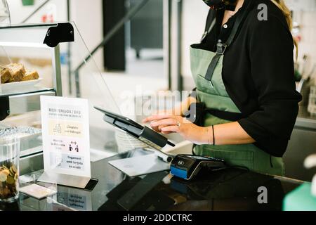 woman wearing apron and face mask using digital tablet while working at coffee shop Stock Photo