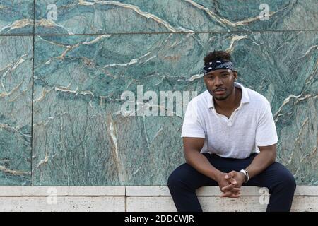 Young man wearing headscarf while sitting against wall Stock Photo