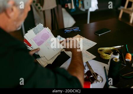 Mature male tailor looking at fabric swatch in work studio Stock Photo
