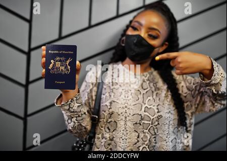 African woman wearing black face mask show Mauritius passport in hand. Coronavirus in Africa country, border closure and quarantine, virus outbreak co Stock Photo