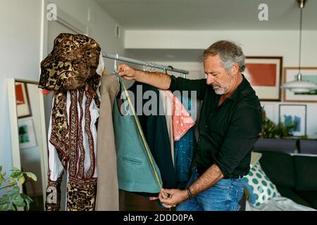 Mature male tailor measuring jacket with measuring tape at work studio Stock Photo