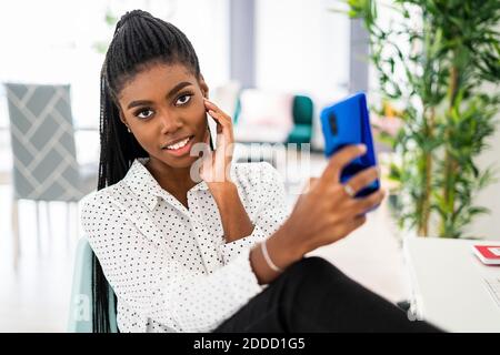 Young female entrepreneur taking selfie on smart phone while sitting at home Stock Photo