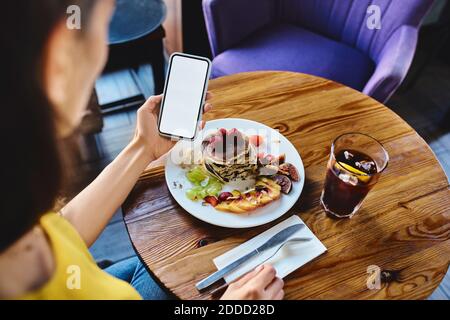 High angle view of young female with pancake using smart phone at table in cafe Stock Photo
