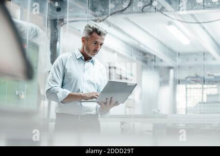 Thoughtful male engineer using laptop while standing in industry Stock Photo