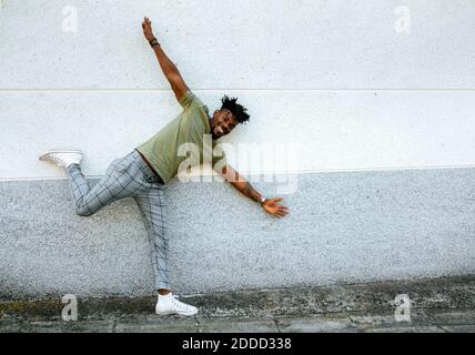 Smiling mid adult man with arms outstretched dancing on footpath against wall Stock Photo