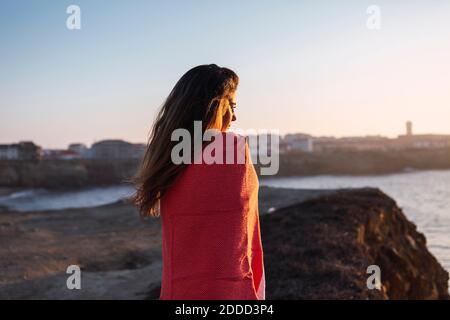 Young woman in covered shawl looking at view while standing at beach Stock Photo