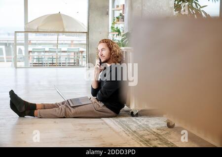Man talking on smart phone sitting with laptop in living room at home Stock Photo