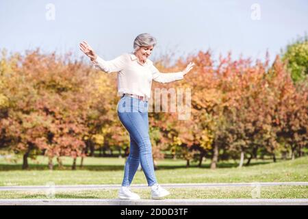 Smiling woman with arms outstretched walking on edge of street road at city Stock Photo