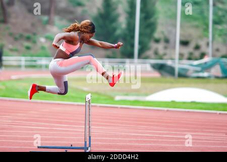 Young sportswoman jumping over hurdle during training Stock Photo