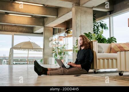 Thoughtful man using laptop while sitting on floor at home Stock Photo