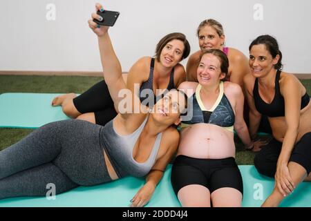 Group of pregnant woman taking selfie on smart phone while sitting at yoga studio Stock Photo