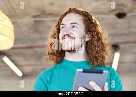 Male hipster with long hair looking away while using digital tablet at home Stock Photo