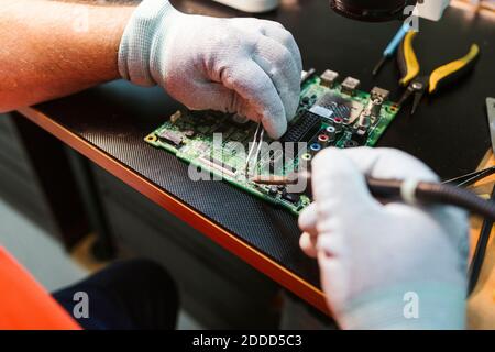 Technician soldering circuit board of electrical component at workbench in electronics repair shop Stock Photo