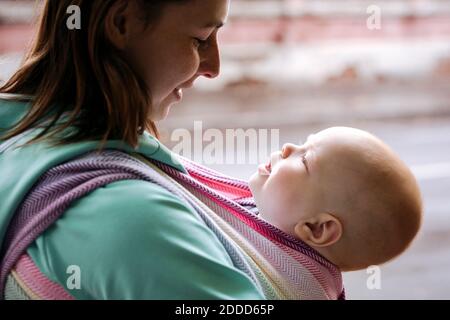 Close-up of mother carrying baby wrapped in blanket standing on sunny day Stock Photo