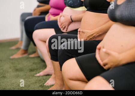 Midsection of pregnant woman sitting with hands on stomach at yoga studio Stock Photo