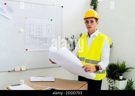 Confident young male engineer holding blueprint at office Stock Photo