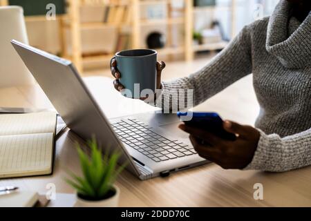 Female entrepreneur holding coffee cup and smart phone while sitting at home Stock Photo