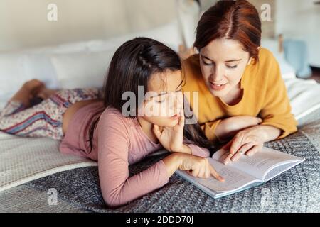 Girl and woman reading book while lying on bed at home Stock Photo