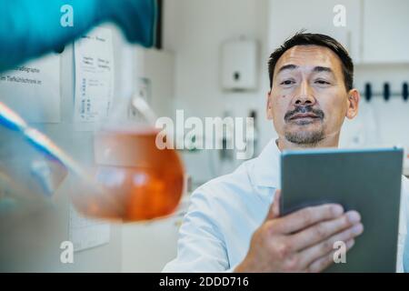 Scientist looking at liquid flask while using digital tablet at laboratory Stock Photo