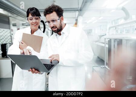 Smiling female scientist looking at male technician using laptop in laboratory Stock Photo