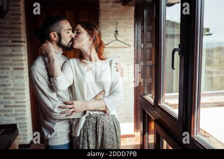 Couple kissing while standing by window at home Stock Photo