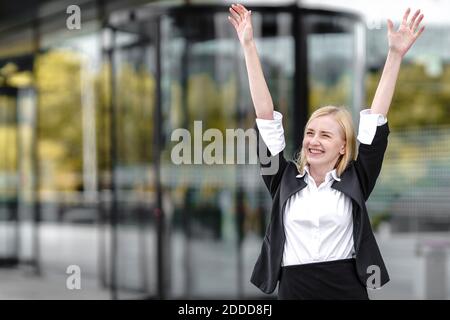 Smiling young woman with hand raised standing against building Stock Photo