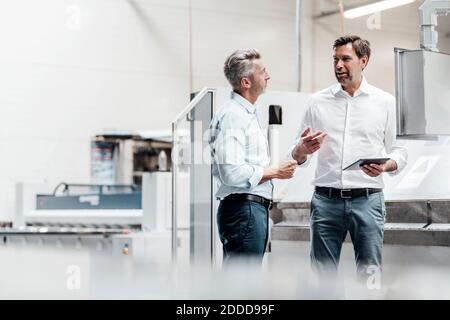 Smiling engineers discussing over digital tablet while standing in industry Stock Photo