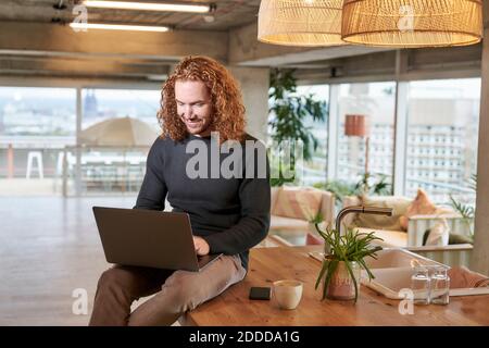 Smiling redhead man using laptop sitting on table at home Stock Photo
