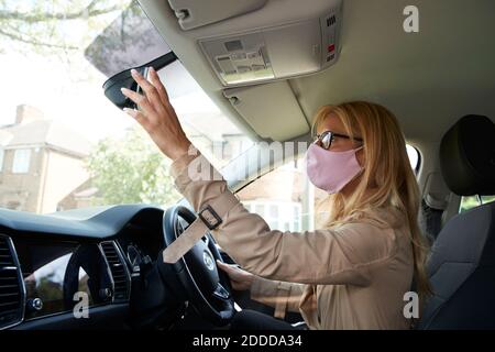 Mature woman adjusting rear view mirror while sitting in car Stock Photo