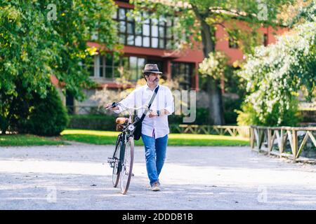 Mature man with bicycle walking on footpath in public park Stock Photo