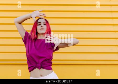 Confident young woman with dyed hair dancing against yellow wall Stock Photo