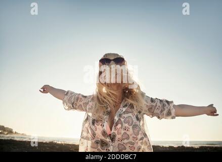 Carefree young woman covering face with hair while dancing at beach against clear sky Stock Photo